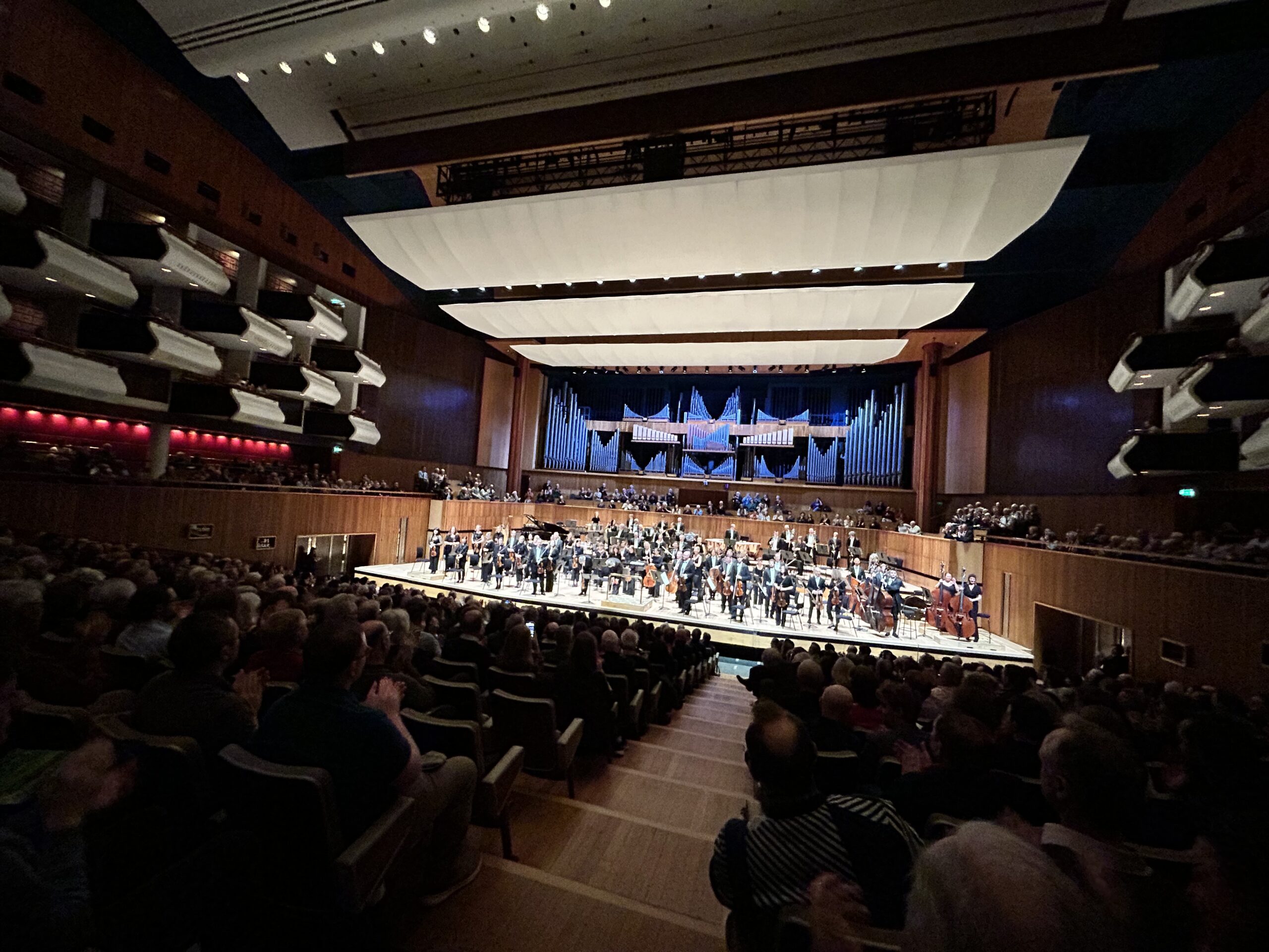 Interior of the Royal Festival Hall with an orchestra on stage and people sat in darkness in the auditorium.